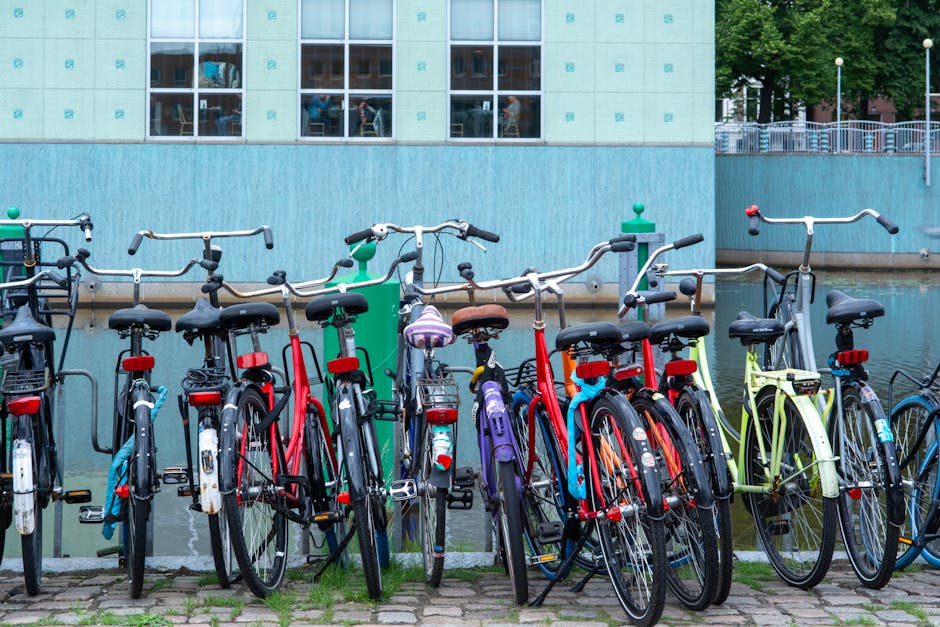 A row of colorful bicycles parked by a canal in a city environment on a clear day.