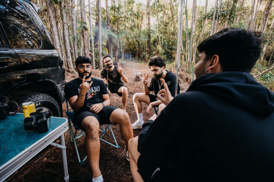 Four men sitting and chatting during a daytime camping trip in the forest.