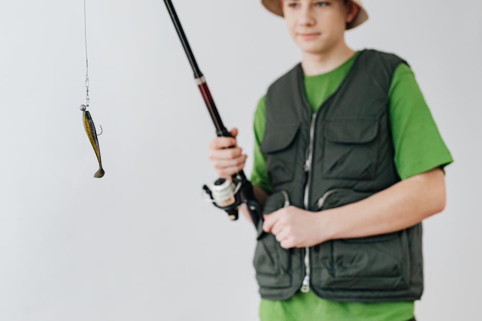Teen boy in a bucket hat holding a fishing rod with a lure, showcasing a fishing hobby.