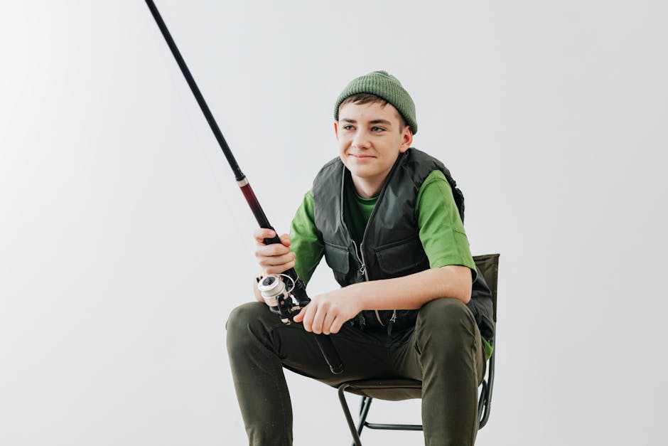 Teenage boy in green outfit holding a fishing rod, sitting on chair, white background.