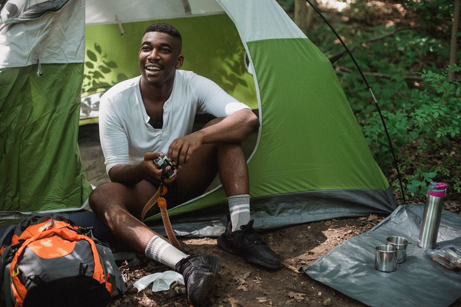Camper sitting outside his tent with sleeping gear and a backpack