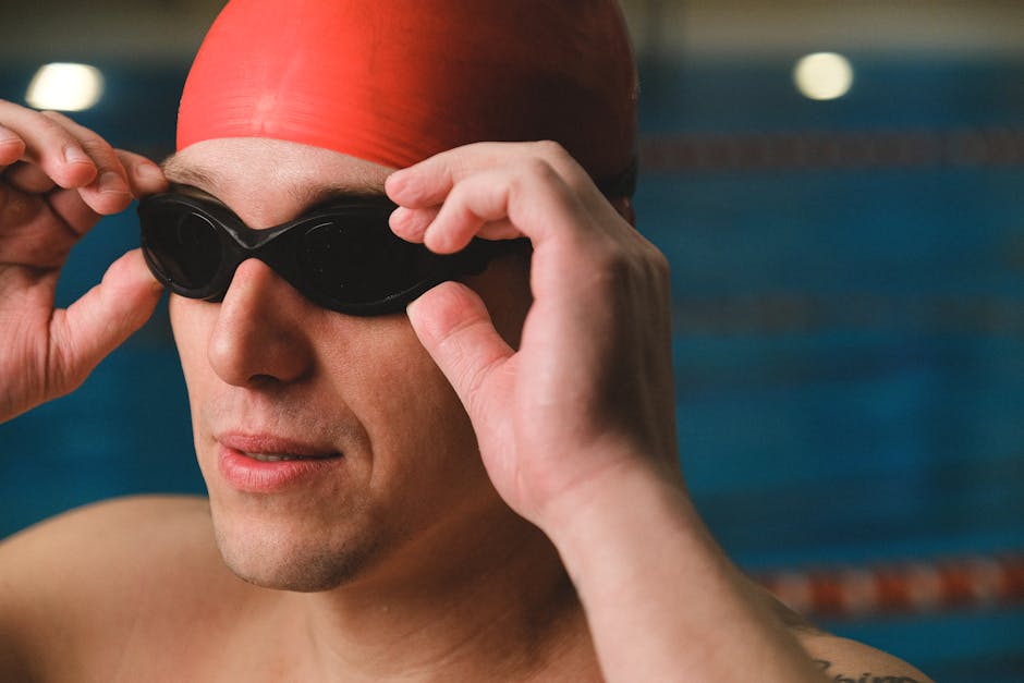 A male swimmer adjusts his goggles, focusing before a swim in an indoor pool.