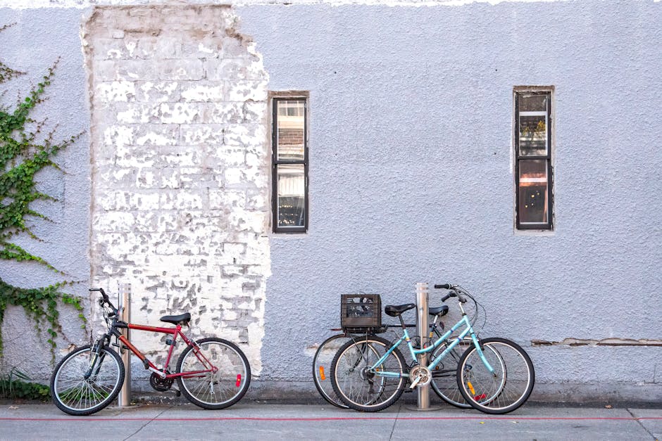 Two bicycles lean against a textured, partially painted brick wall on a sunny day, capturing urban charm.