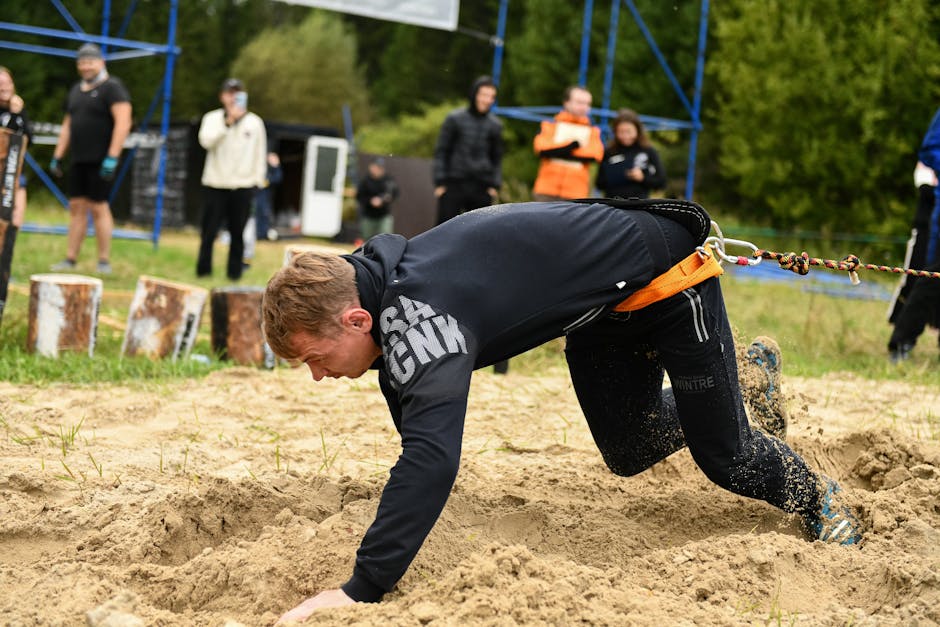 Man demonstrating strength as he crawls in a sand obstacle course with a body harness outdoors.