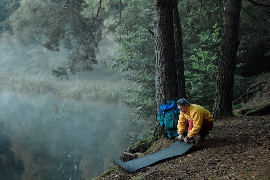 A hiker sets up camp by a serene, misty forest lake at dawn, surrounded by nature.
