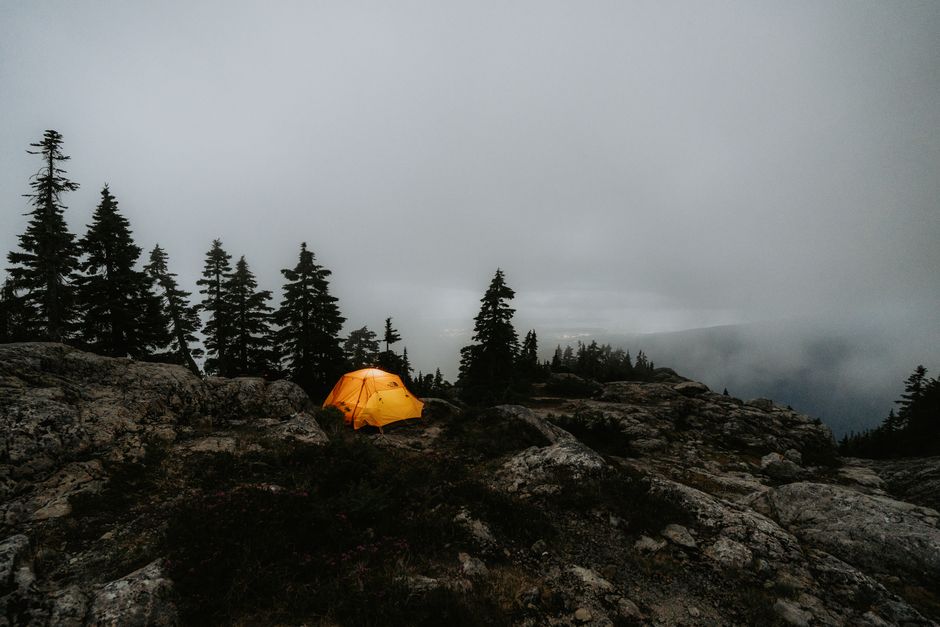 Orange tent on a foggy mountainside at dawn after a cold night
