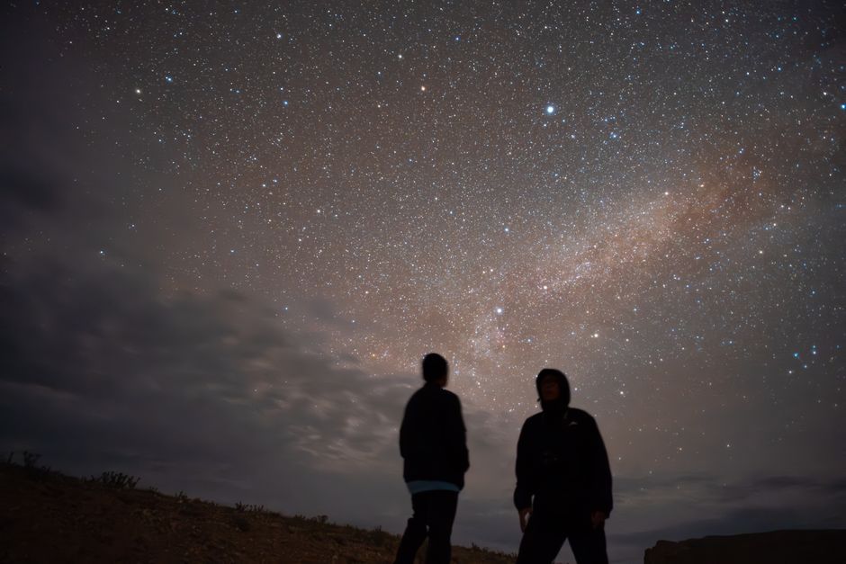 Two people silhouetted against a bright starry night, gazing at the Milky Way.