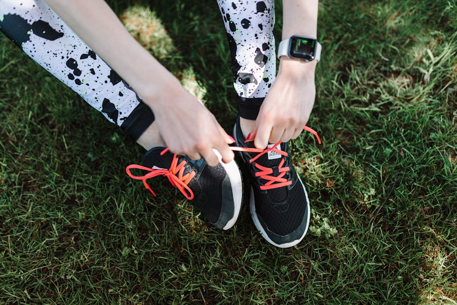 Close-up of a runner tying shoelaces on black sneakers with red laces, outdoors on grass.