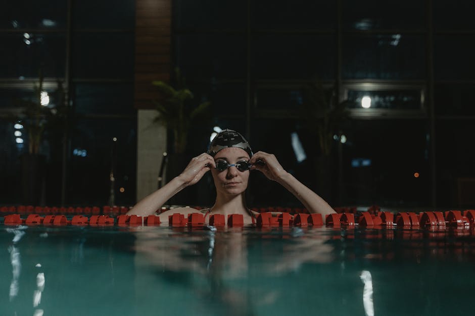 Woman swimmer adjusting goggles in an indoor swimming pool, ready for a swim.