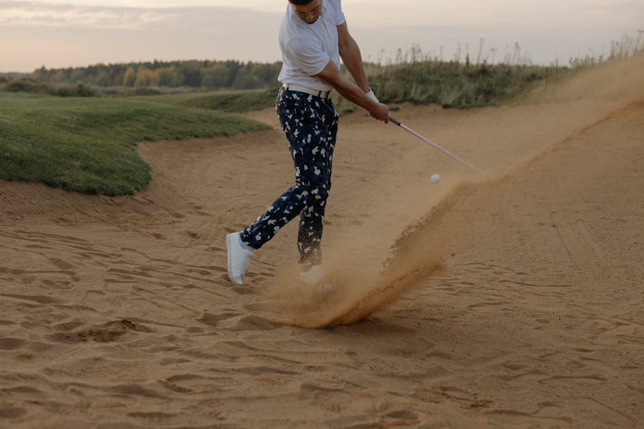 A golfer in a sand trap skillfully hits the ball on a sunny golf course.