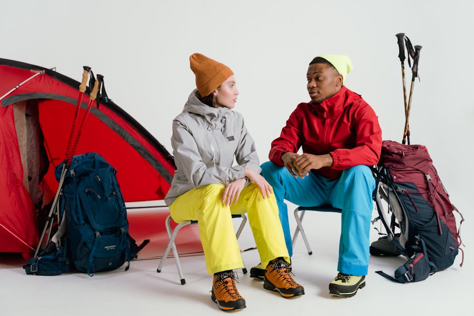 Two campers sit with hiking gear and tent in a studio setting.