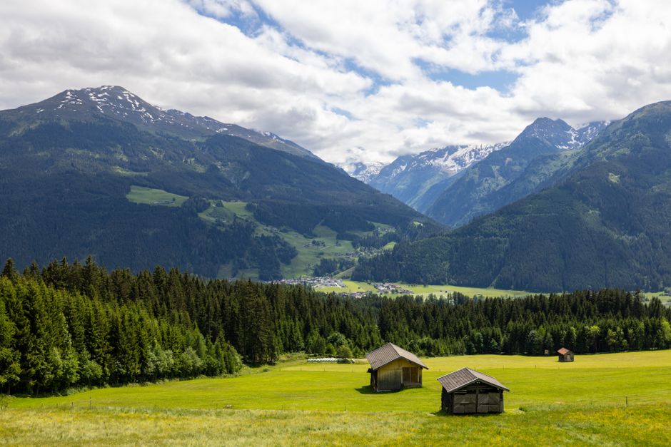 Wooden huts in a green alpine meadow below mountain peaks